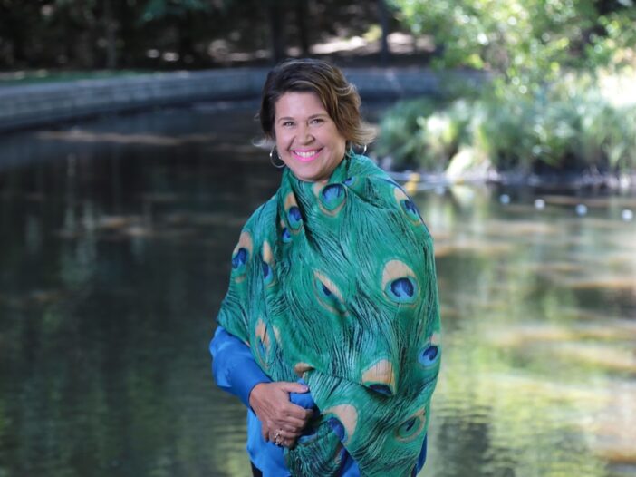 Janice Landry wears a colourful shawl and stands before a lake of matching colours.